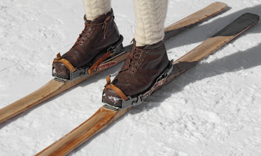The history of ski bindings: an image showing traditional early wooden with a simple leather strap binding across the toe of a lace up leather boot