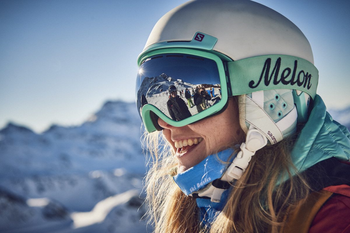 Woman skiing with helmet and reflection of friend in goggles